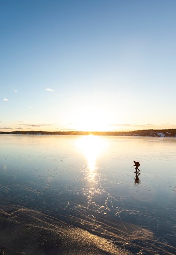 En istäckt sjö vid soluppgång med en ensam långfärdsskriskoåkare